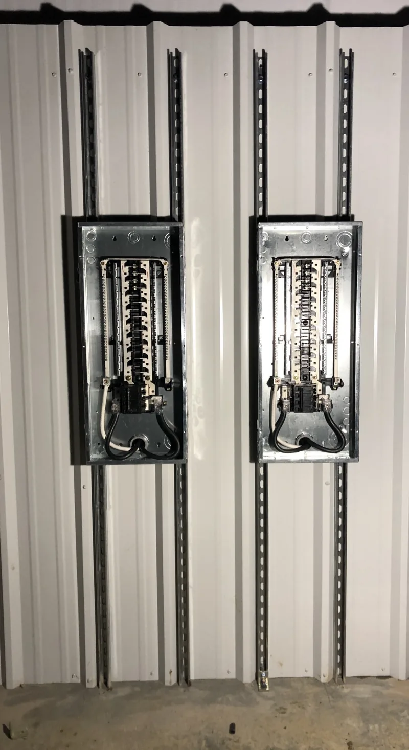Two new panels side by side on a metal building wall, conduit run straight, by DC Electric