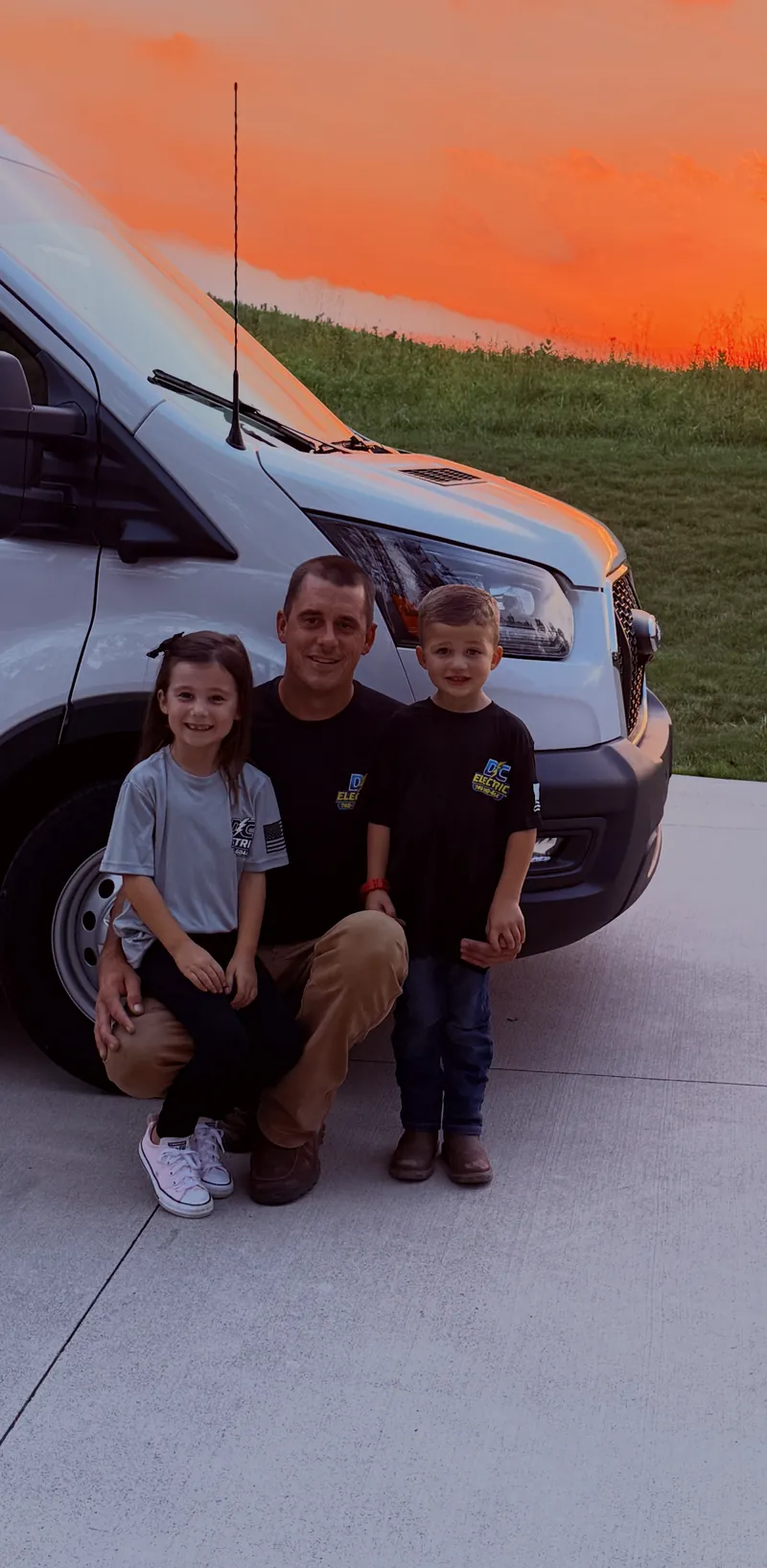 The owner of DC Electric crouched beside the work van with his two children