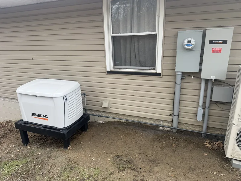 A Generac standby generator beside a sided house with the meter and transfer switch on the wall