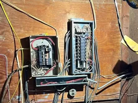 Before: two old panels on a plywood wall with cables run loose in every direction
