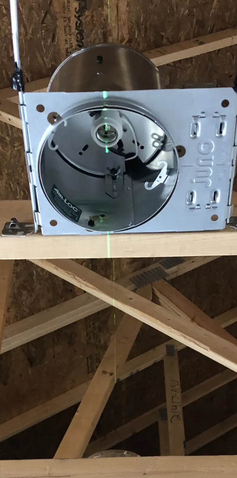 A laser line running across a recessed light can in a joist bay, on a DC Electric job