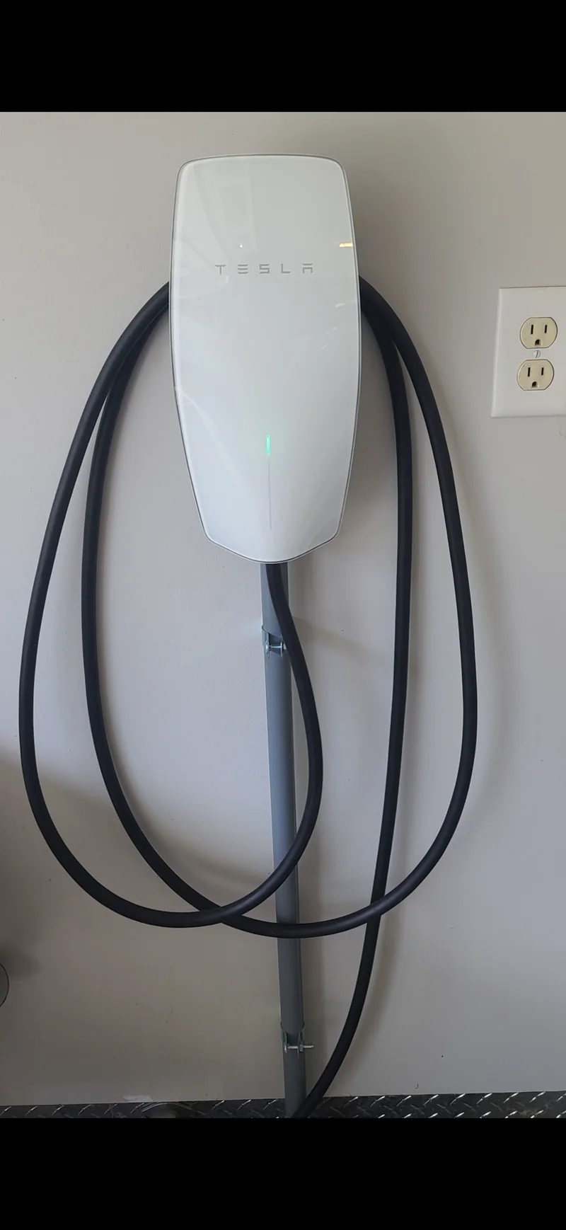 A Tesla Wall Connector on a garage wall with the cable coiled on its hook, installed by DC Electric for a customer